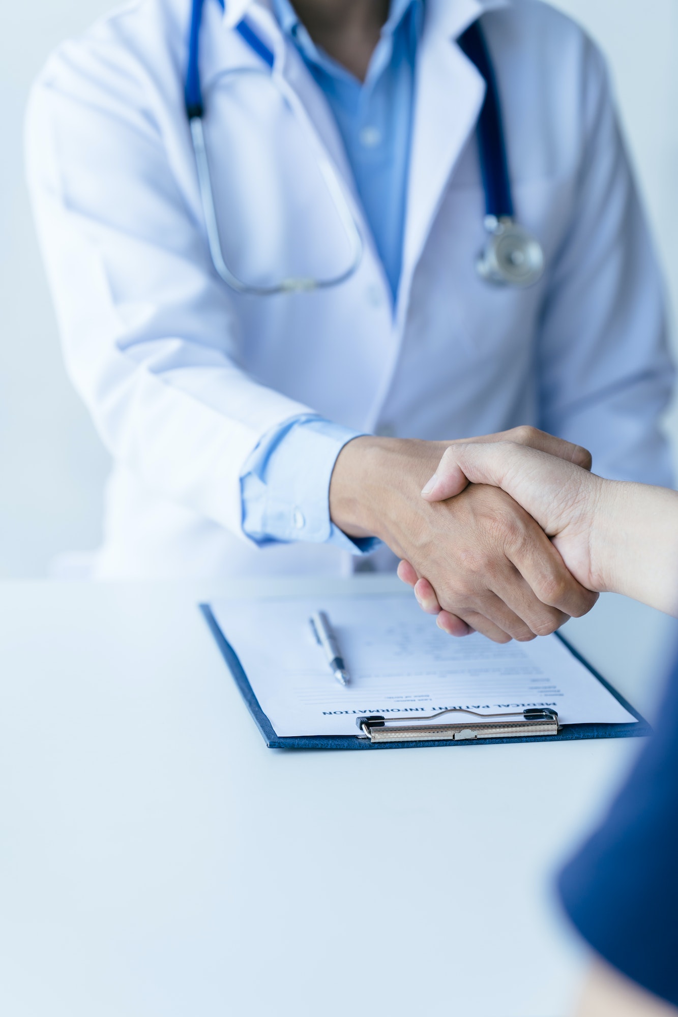 Doctor and patient shaking hands in the office, they are sitting at desk, hands close up